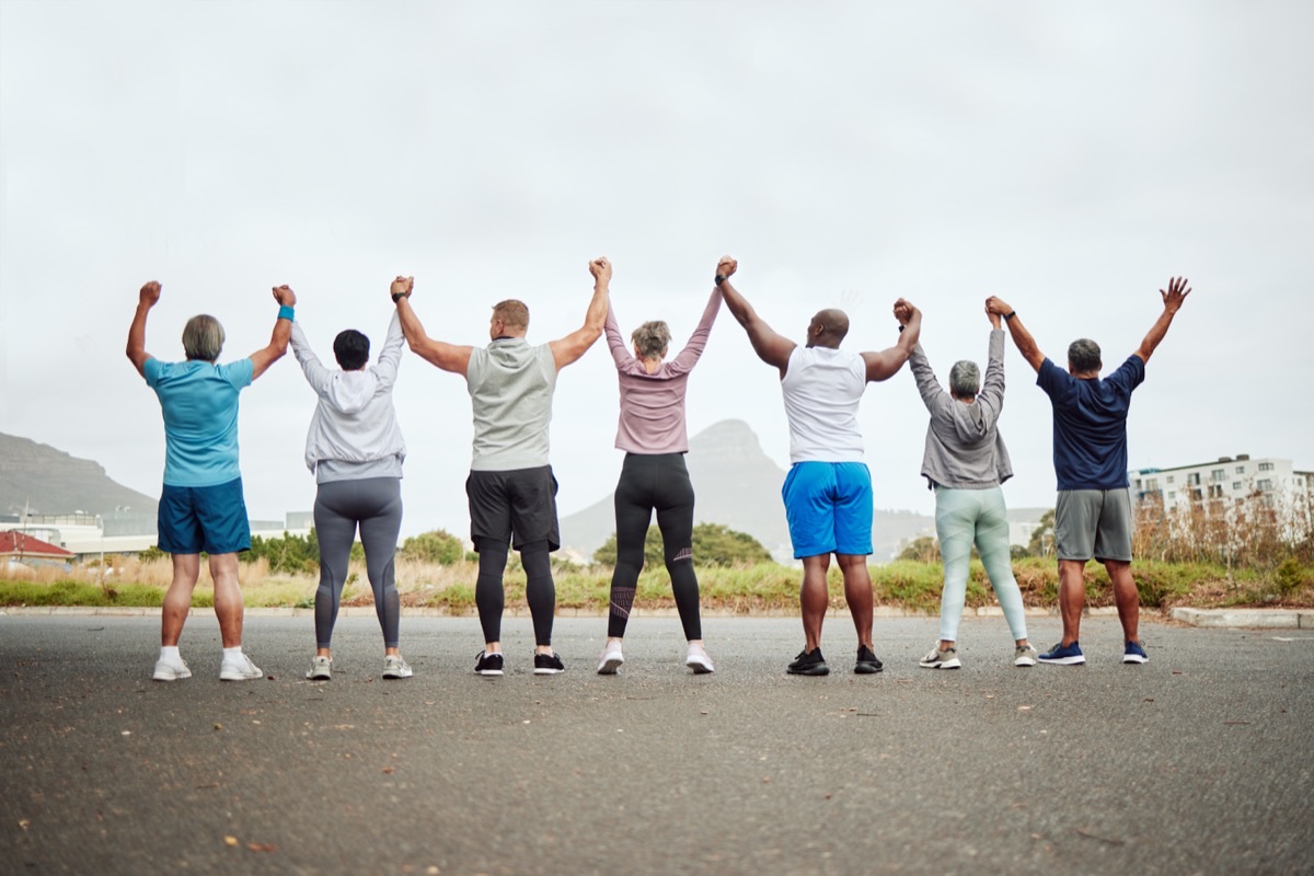 A group of people standing in a row outdoors, holding hands raised in the air.