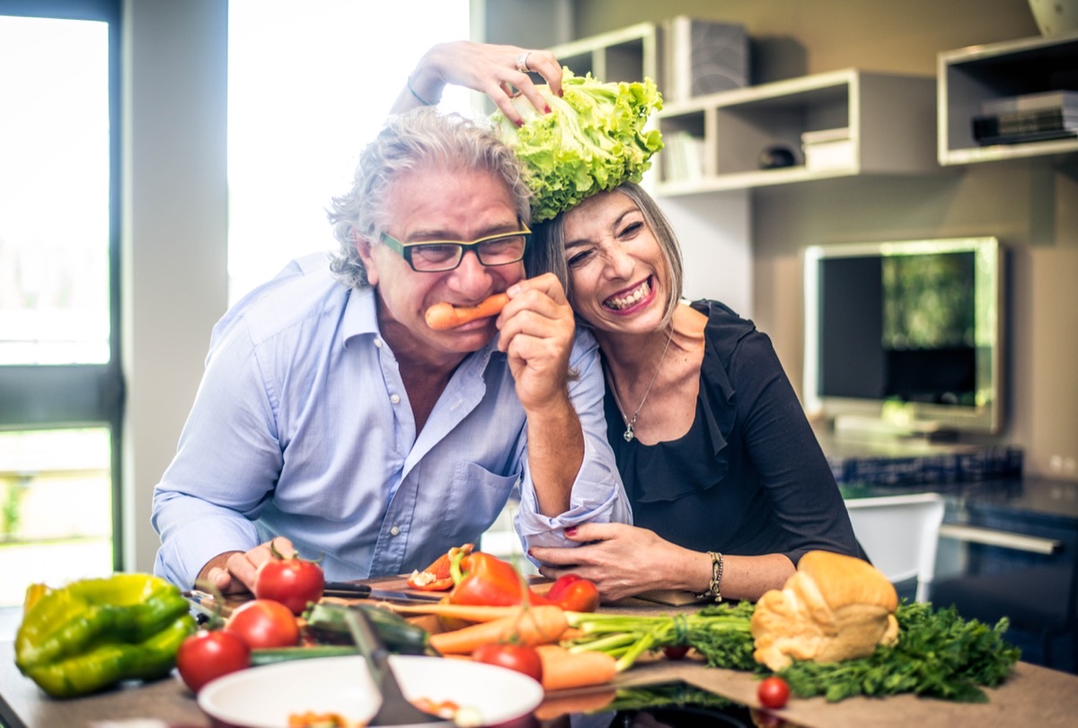 A couple laughing together while preparing fresh vegetables in the kitchen.