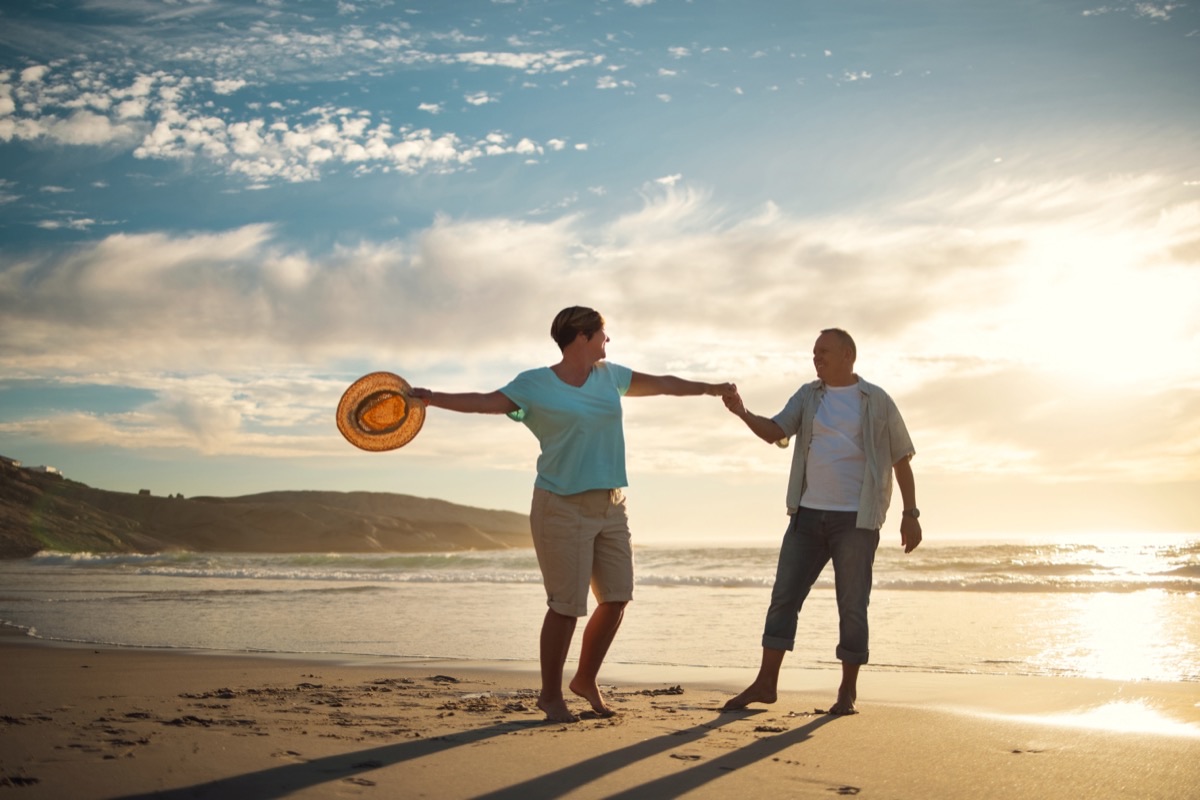 A couple holding hands and laughing together on the beach at sunset.