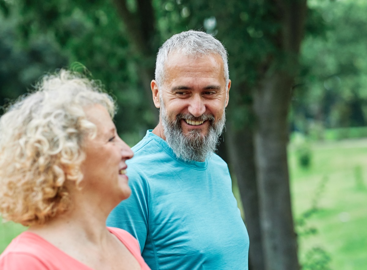 A man and woman smiling and talking together outdoors.