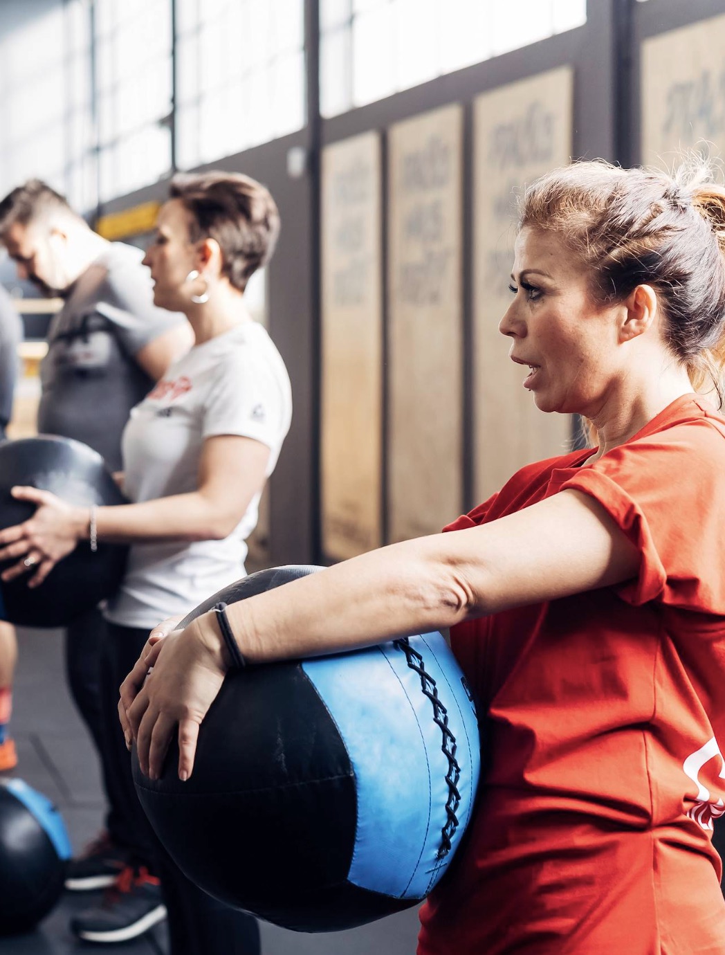 A woman resting against a medicine ball during a gym class, with other participants exercising behind her.